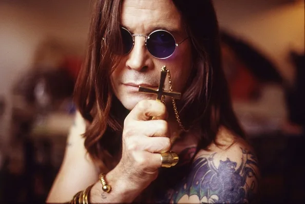 Ozzy Osbourne holding a cross necklace and wearing sunglasses.