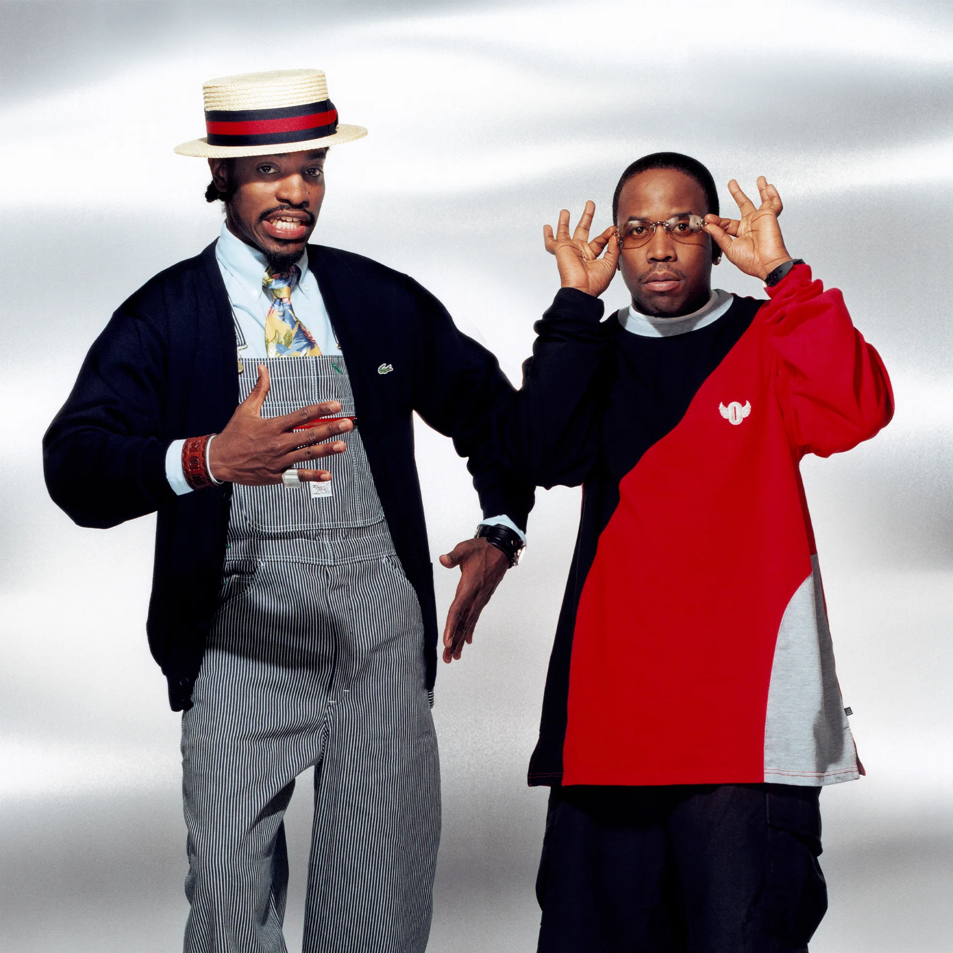 OutKast André 3000 and Big Boi 1990s promotional portrait – André 3000 wearing a boater hat and striped overalls, Big Boi in a red and black color-block sweatshirt adjusting his glasses