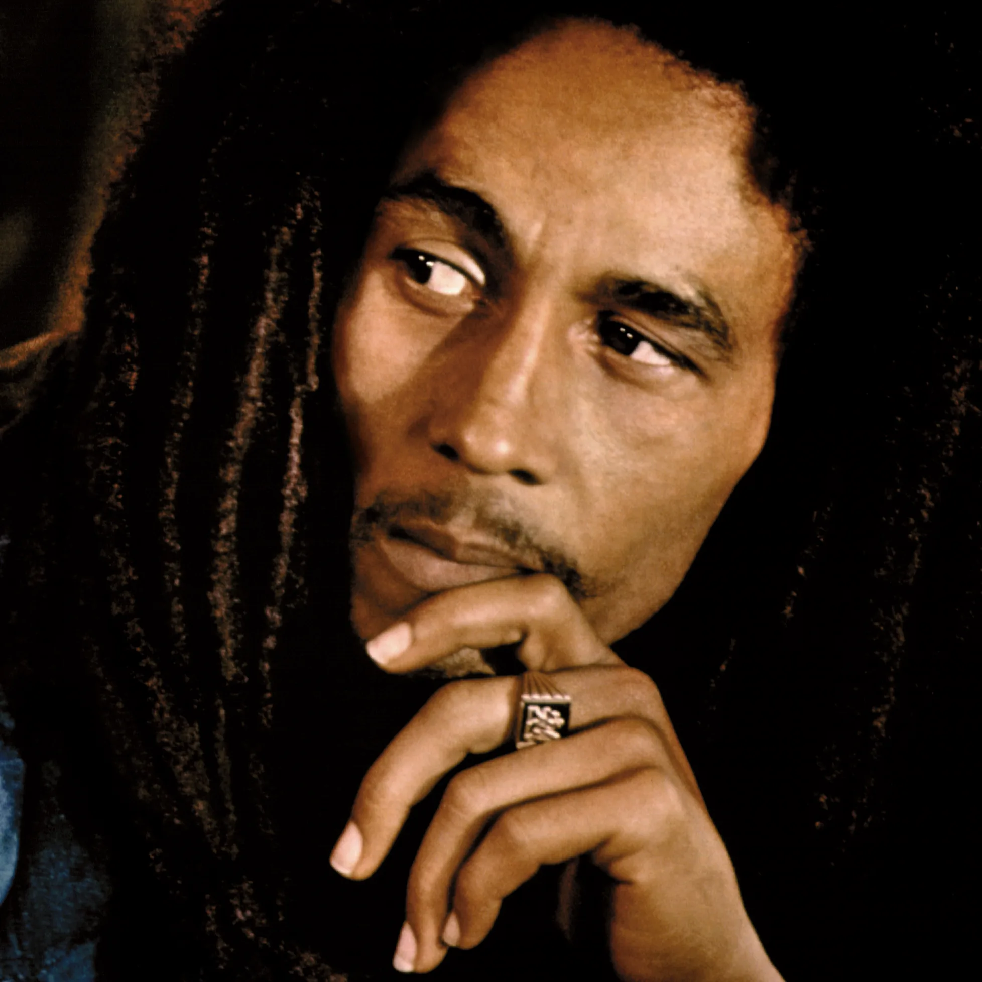 Bob Marley close-up portrait with dreadlocks, hand on chin wearing a large ring, thoughtful expression looking to the side – iconic reggae legend.