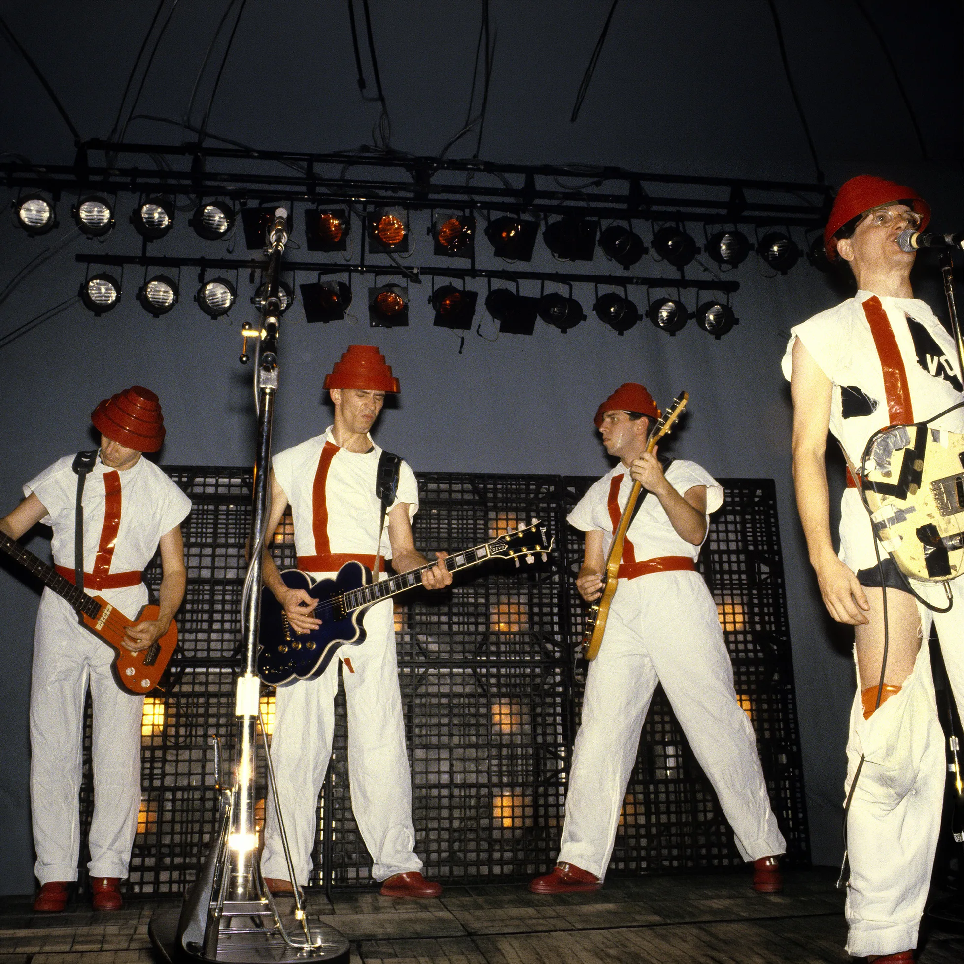 Devo performing live on stage in iconic red hats and white outfits.