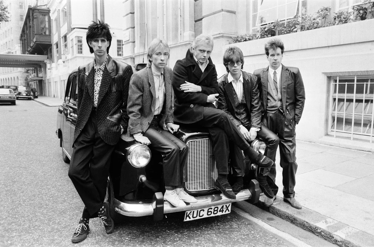 The Cars band photo, seated on the hood on a car.