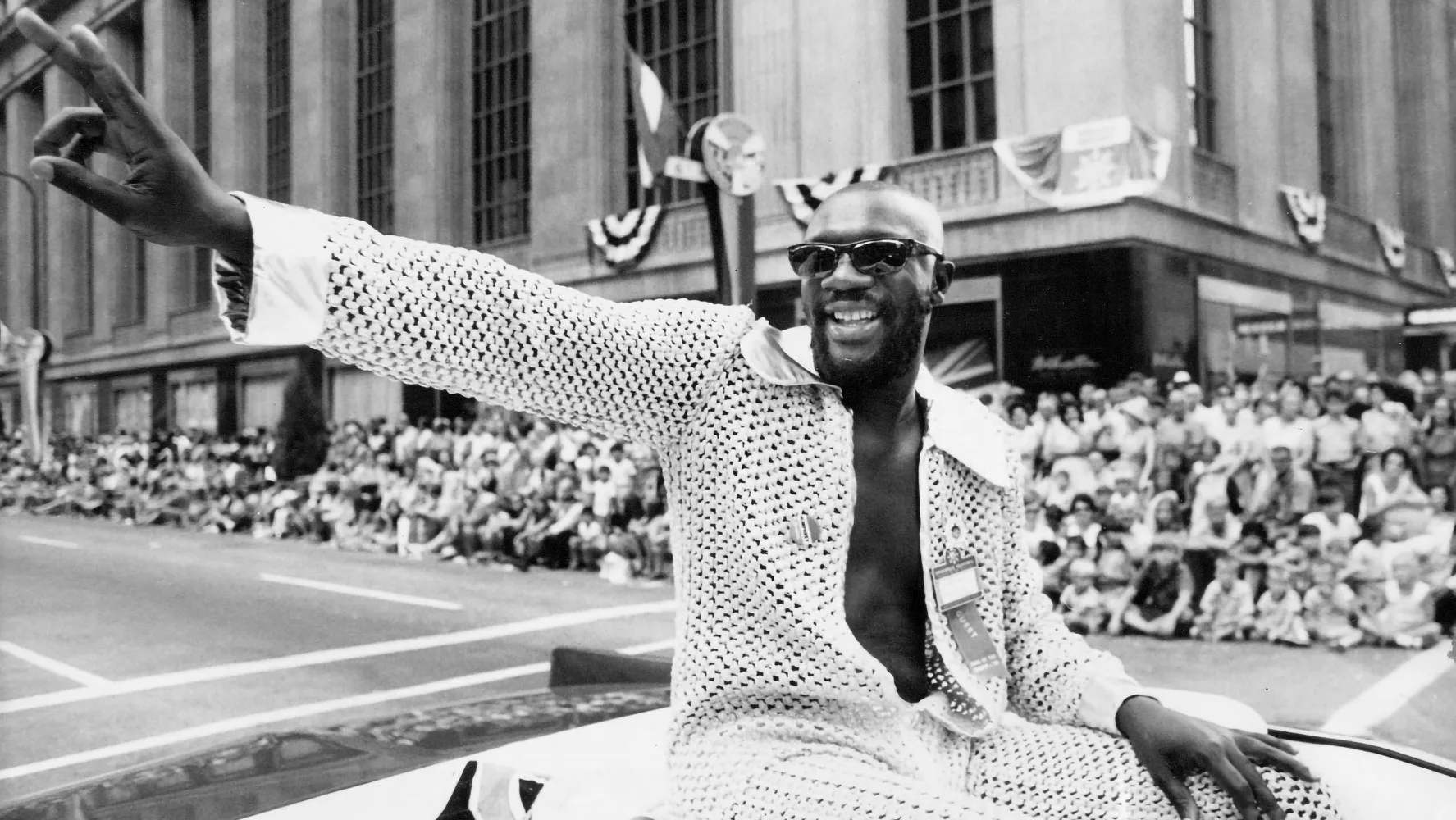 Issac Hayes waving to fans from the back of a convertible.