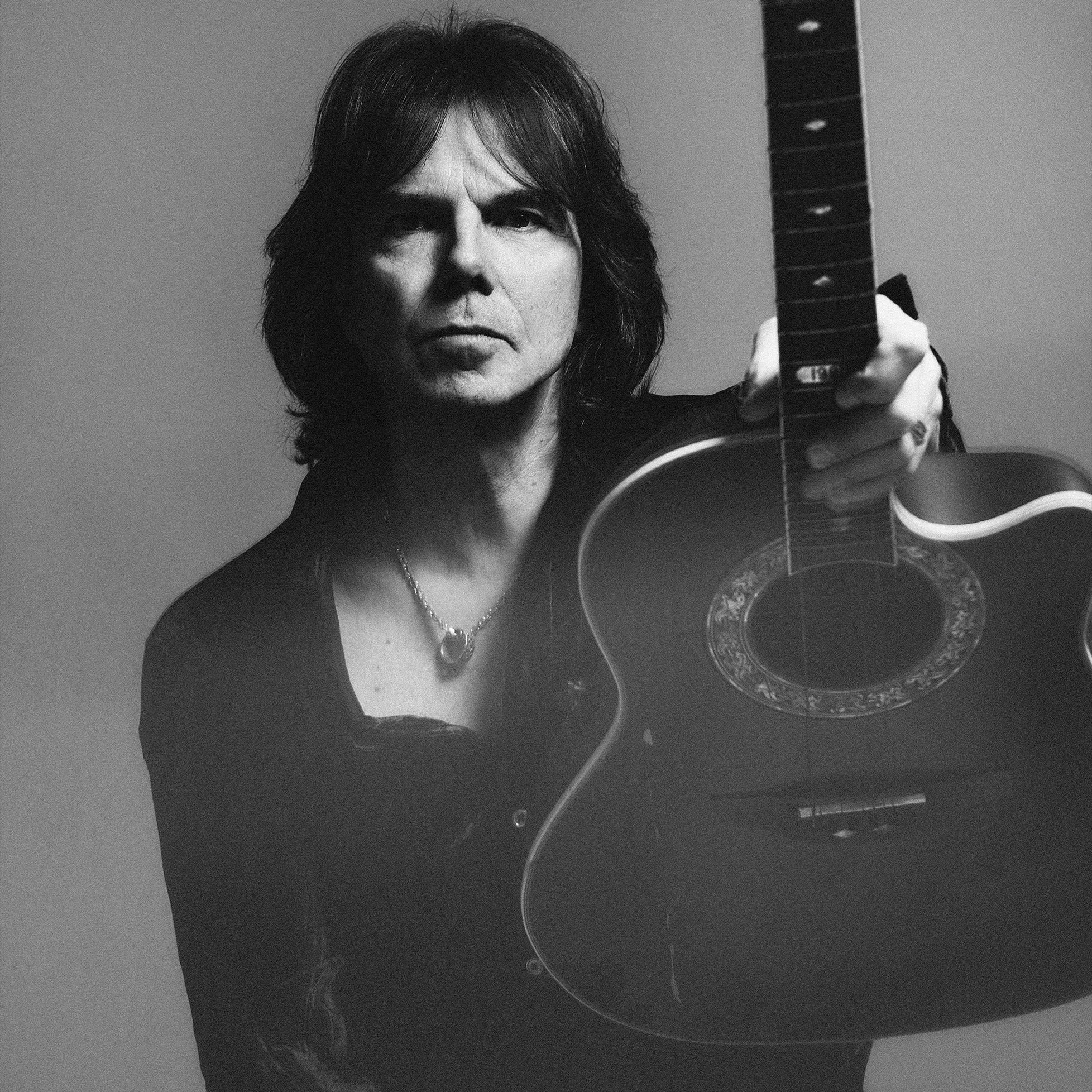 Joey Tempest holding an acoustic guitar, black and white portrait.
