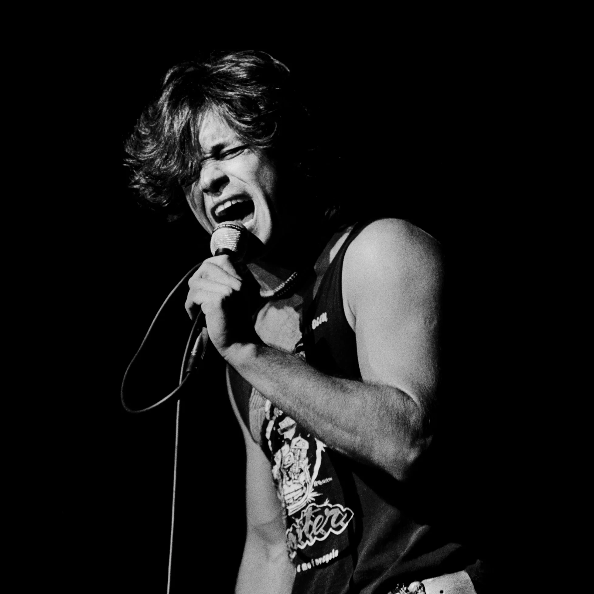 John Mellencamp singing passionately into a microphone on stage, black and white photo.