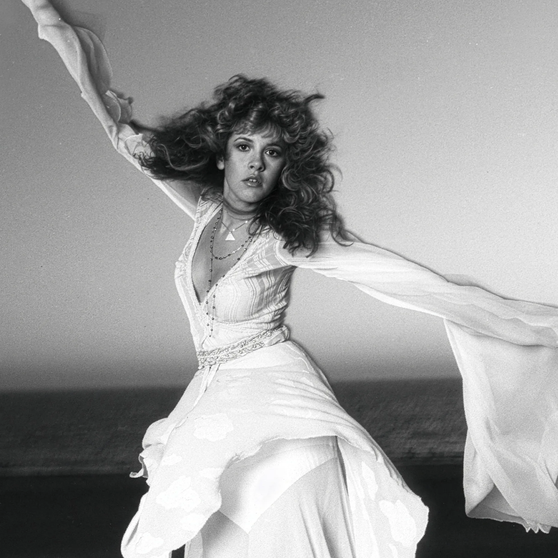 Stevie Nicks in a dramatic flowing white dress with arms outstretched.