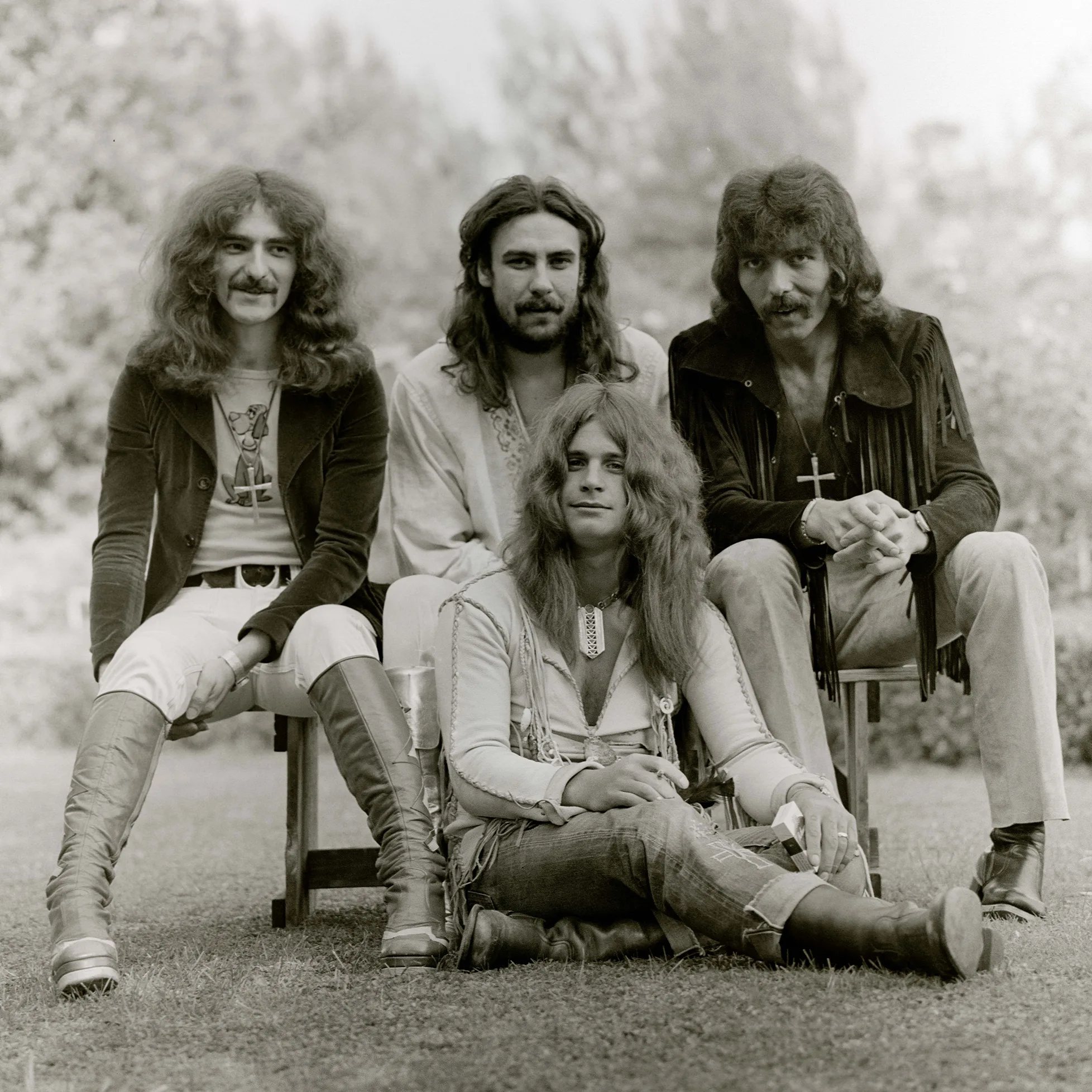 Black-and-white portrait of Black Sabbath members seated outdoors in 1970s attire.
