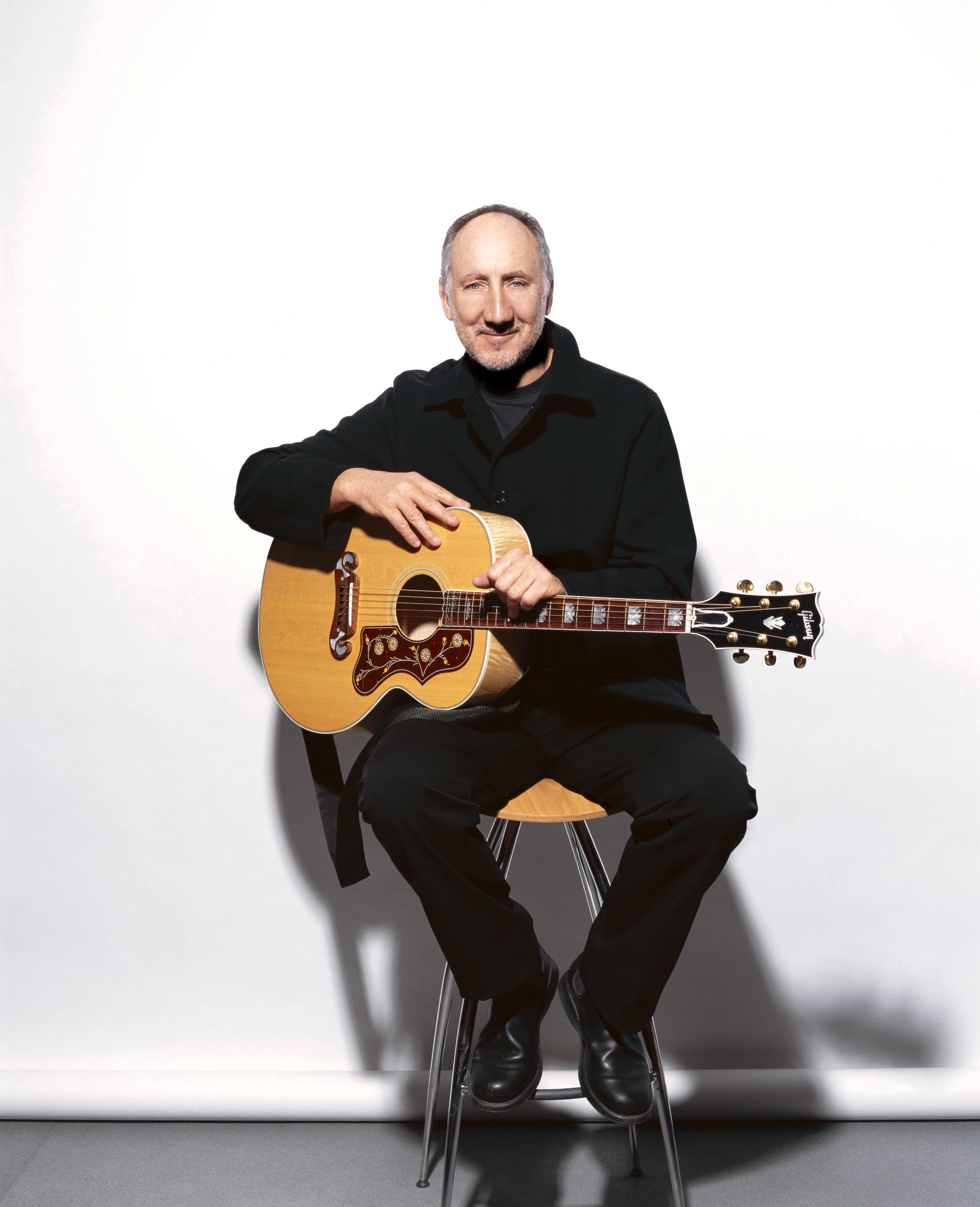 Pete Townshend sitting on a stool, holding a guitar.